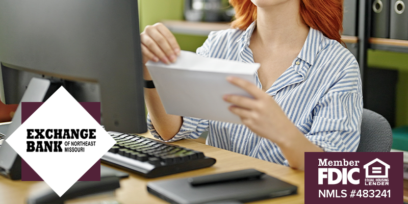 Woman opening envelope in front of her computer at her desk